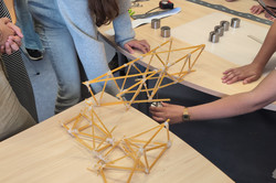 Mehrere Personen bauen auf einem Tisch eine Brücke aus Spaghetti und Schnur