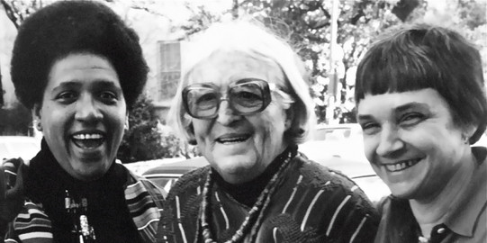 Three women stand next to each other and laugh into the camera
