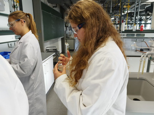 Eine MinTU-Teilnehmerin, die Schutzbrille und Laborkittel trägt, macht einen Fingerabdruck auf eine Agarplatte.