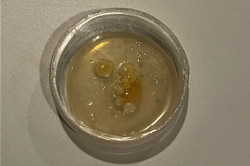 Nahaufnahme eines durchsichtigen Behälters mit gelblich-transparenten Flüssigkeitstropfen auf einer hellen Oberfläche