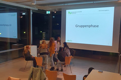 ‘Group phase’ is written on a screen and a group forms a circle of chairs in front of it. 