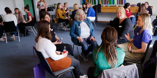 In einem großen Seminarraum sitzen Frauen in mehreren kleinen Gesprächsrunden zusammen.