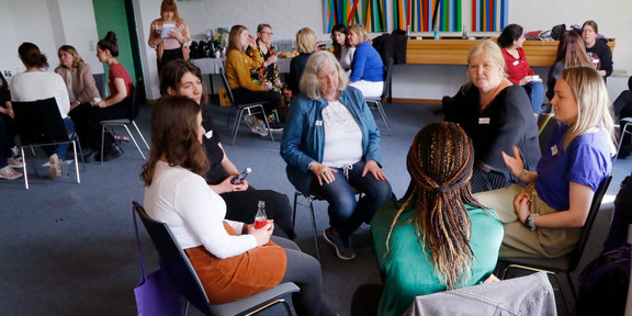 In einem großen Seminarraum sitzen Frauen in mehreren kleinen Gesprächsrunden zusammen.