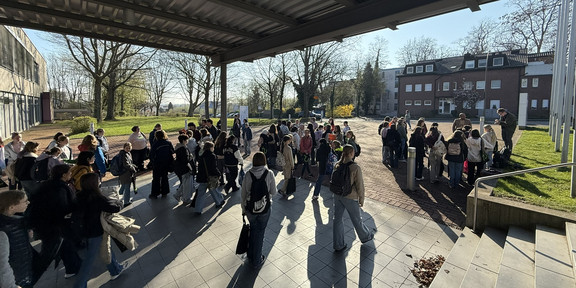 Many girls stand in small groups on a square outside a building.