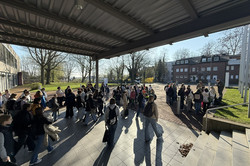 Many girls stand in small groups on a square outside a building.