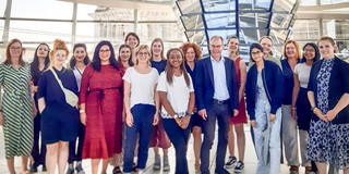 Gruppenfoto: 17 Frauen und ein Mann im Anzug, im Hintergrund: Reichstagskuppel