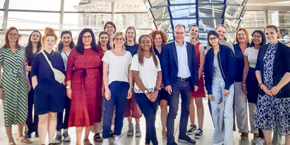 Group photo: 17 women and one man in a suit, in the background: Reichstag dome