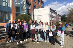 12 Mentees und ihre Mentorinnen stehen vor einem Gebäude. Alle lächeln in die Kamera. 