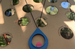 Holzbrett mit mehreren runden Löchern und einem blauen hängenden Ring mit einem pinken Spielstein darin.