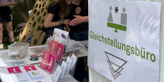 An outdoor tent booth with informational materials and green paper decorations at a summer festival.