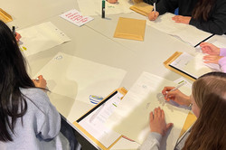 Four girls sit at a table and draw sheets of paper. 