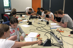 Eine Gruppe sitzt zusammen und lötet mit Lötkolben und Platinen
