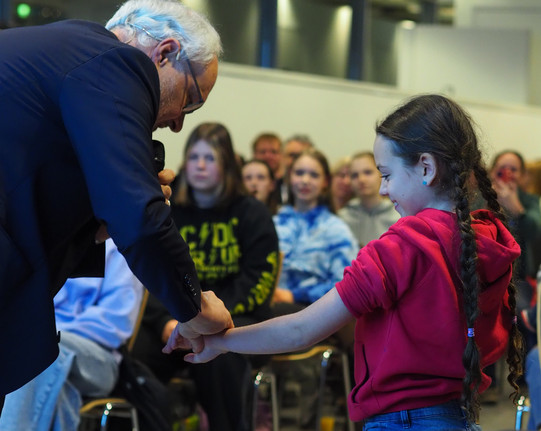 Rechts steht ein Mädchen. Der Ärmel ihres Pullovers ist am linken Arm hochgekrempelt. Sie strekt den Arm zu einem Mann, der an dem Unterarm Elektroden befestigt. 
