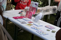 Zelt mit Infostand, auf dem Flyer, Buttons und Broschüren liegen, im Hintergrund Personen und grüne Papierdekoration.