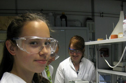 Ein Mädchen im Kittel und mit Schutzbrille steht im Labor und stellt Pastillen her