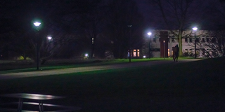 Dark path on campus, only a few lamps are lit.
