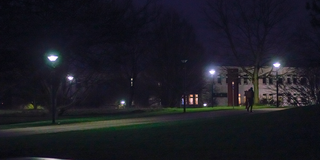 Dark path on campus, only a few lamps are lit.