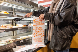 Eine Person bedient sich in der Cafeteria, die Brötchentüte hat die Aufschrift "Gewalt kommt mir nicht auf den Campus"