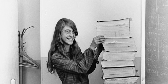 The photo shows Margaret Hamilton with the printout of the flight software algorithm. The stack is as big as she is.