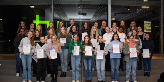 A group of schoolgirls stand on a staircase and hold their certificates in their hands.