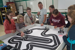 Eine Gruppe von Mädchen steht an einer Strecke, die ein Lego-Roboter entlang fahren soll. Die Mädchen haben den Roboter eigens progammiert