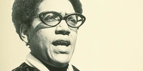 Portrait of a black woman with glasses and a short afro (Audre Lorde) as she speaks 