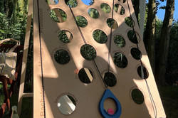 Großes Spielbrett mit unterschiedlich großen runden Löchern und einem blauen Ring an Schnüren im Freien.