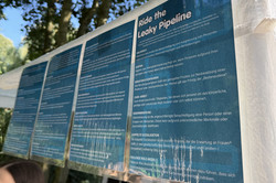 Mehrere blaue Informationsplakate mit weißem Text hängen an einem weißen Pavillion im Freien unter Bäumen.