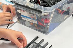 Zwei Hände halten eine Konstruktion aus Lego in der Hand. Daneben steht eine Kiste mit viele verscheidenen Legosteinen. 