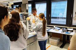 In the chemistry lab, a girl and the workshop leader are standing at a press with a crank. The girl turns the crank.