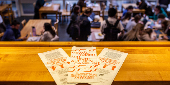 Foreground: sandwich bags with the inscription ‘Gewalt kommt mir nicht auf dem Campus’ (‘Violence doesn't come on campus’). Background: Students in the cafeteria