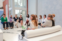 Mehrere Frauen sitzen in einem hellen Raum auf weißen Sofas im Halbkreis.