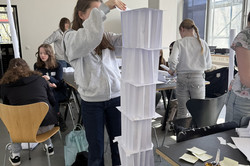 A girl builds a tower out of white sheets.The tower reaches up to her head. 