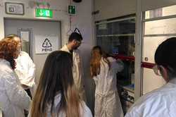 A girl stands in front of the disc, her hands behind the disc, handling the equipment. The workshop leader is standing next to her, four other girls are watching. 