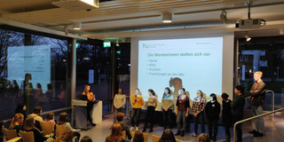 Students stand in front of a projector screen and introduce themselves to pupils.