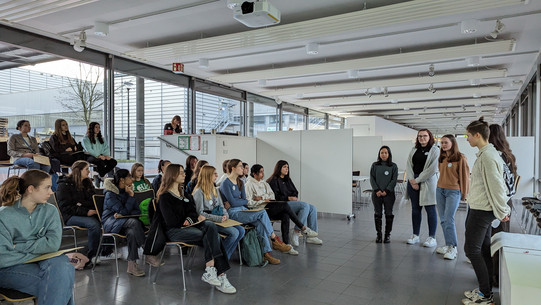 Studentinnen stehen vor einer Gruppe von Schülerinnen