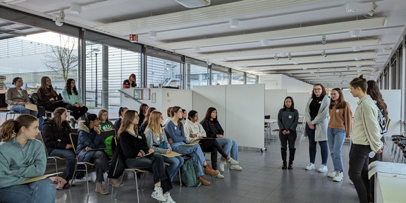 Studentinnen stehen vor einer Gruppe von Schülerinnen