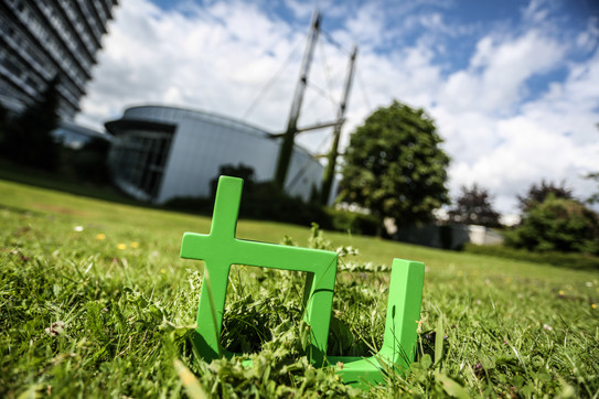 TU logo made of wood in the grass in front of the Audimax