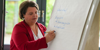 Eine Frau in rotem Sakko schreibt etwas an eine Flipchart