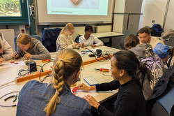 Acht Mentees sitzen in Zweierteams zusammen und löten gemeinsam einen Radiotransmitter