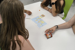 Vier Mädchen sitzen an einem Tisch. Auf dem Tisch liegt eine ausgedruckte Weltkarte und daneben ein Päckchen "Nutella & go"