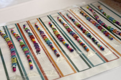 Nahaufnahme von mehreren Reihen von Armbändern mit buntn Perlen mit Buchstaben auf einer Unterlage.
