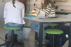 Mehrere Mädchen sitzen an einem Tisch, eine forscht mit einer Taschenlampe nach Eigenschaften von Lichtwellen.