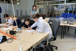 An einem Tisch sitzen vier Mädchen. Jeweils zu zweit löten sie einen Radiotransmitter. 