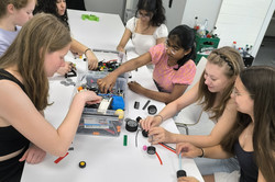 Sieben Mädchen sitzen an einem Tisch und bauen mit Lego. 